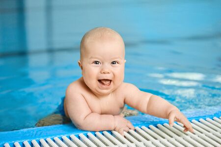 Portrait of happy, smiling little baby boy on edge of swimming pool in water. Kid looks at the camera. Concept active lifestyle of child.の写真素材