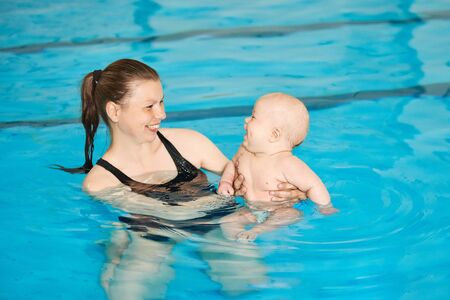 Mother teaching happy little baby to swim in water pool. Swimming lessons for children. Healthy Family Life.の写真素材