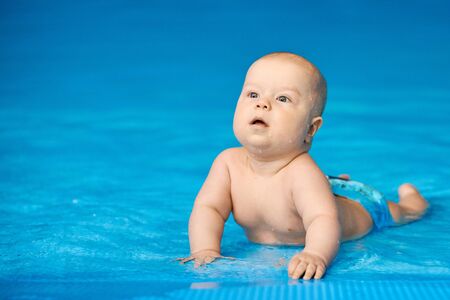 Little baby boy lying in blue swimming pool in water. Concept active lifestyle of child.の写真素材