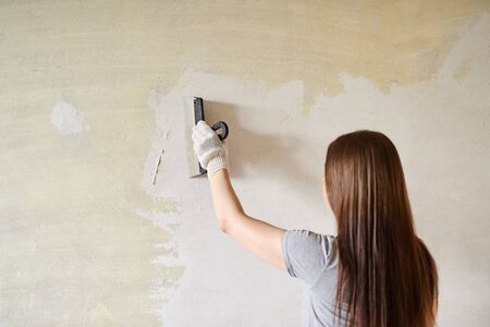 Woman plastering the walls with finishing putty in the room with putty knife or spatula. Repair work, decoration building concept, construction.の写真素材