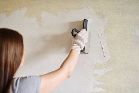 Woman plastering the walls with finishing putty in the room with putty knife or spatula. Repair work, decoration building concept, construction.の写真素材