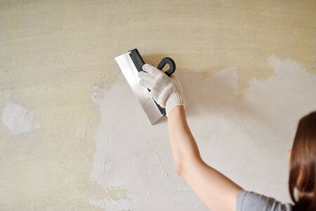 Woman plastering the walls with finishing putty in the room with putty knife or spatula. Repair work, decoration building concept, construction.の写真素材