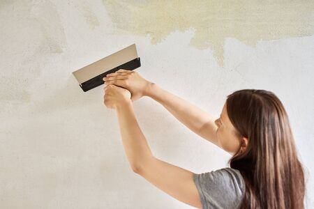 Woman plastering the walls with finishing putty in the room with putty knife or spatula. Repair work, decoration building concept, construction.の写真素材