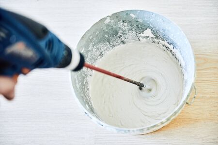 Worker mixing plaster in a bucket for alignment and putty walls of the apartment using an electric drill, close-up.の写真素材