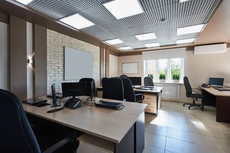 Modern interior design of empty business office space. Equipped workplaces with tables and chairs, computers and phones without employees. Office scene without people.の写真素材