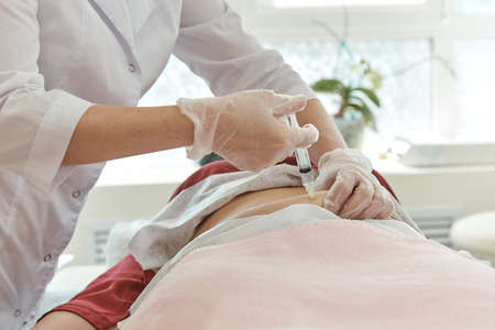 Doctor in white coat and gloves gives an injection into stomach of patient who is lying on couch.の写真素材