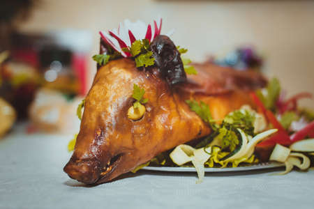Closeup of the head of roasted young pig on plate with vegetables and fresh herbs.の写真素材