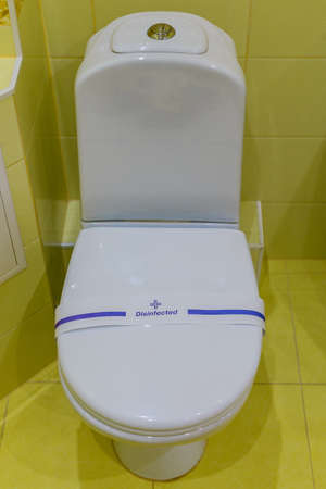 White, clean toilet with the word disinfected is in the bathroom with tiles on walls.の写真素材