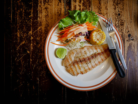 Dolly fish steak plate, knife, and fork for mixed salad on a wooden tableの写真素材