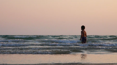 A boy is standing and looking at the waves on the beach.の写真素材