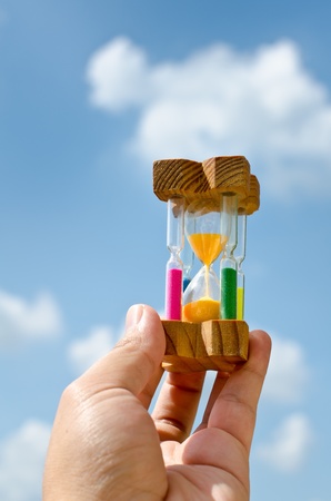 Colorful hourglass sand timer in hand of man on the skyの写真素材