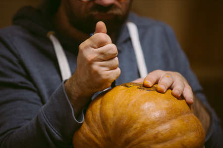 Young man carving face on pumpkin for halloweenの写真素材
