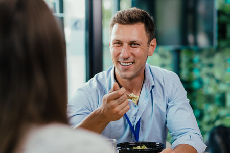 Young businessman eating healthy salad lunch with colleagues in modern office cafeteriaの写真素材