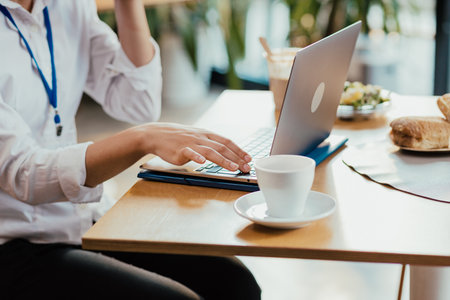 Womans hands typing on laptop during lunch break with coffee and sandwich on deskの写真素材