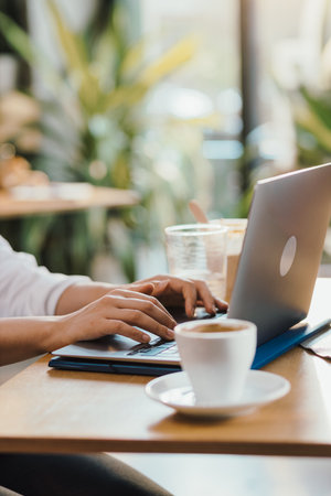 Womans hands typing on laptop during lunch break with coffee and sandwich on deskの写真素材