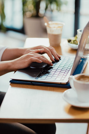 Womans hands typing on laptop during lunch break with coffee and sandwich on deskの写真素材