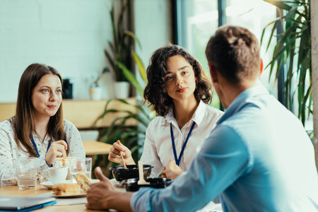 Three young coworkers chatting over healthy lunch in bright office cafeteriaの写真素材