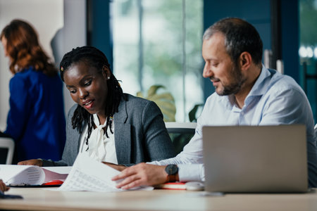 Confident Black Woman Leads Feedback Session Meeting in Modern Open Officeの写真素材