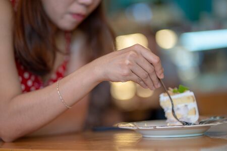 Close up concept hand of woman cut cake by fork in cafe or restaurant backgroundの写真素材
