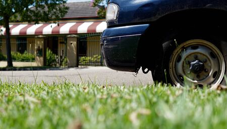 Front side view of car wheel white automobile parking on street beside of green grass sidewalk with house in the background.の写真素材