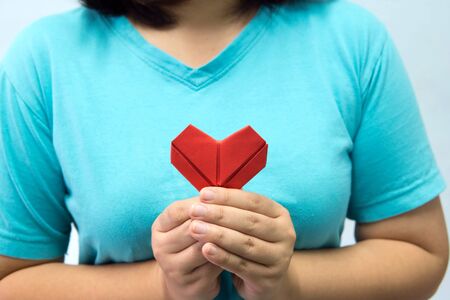 An asian woman holding heart origami in front of her chest. A woman giving red heart paper to...