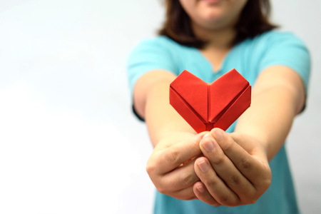 An asian woman holding heart origami in front of her chest. A woman giving red heart paper to someone. Love and give concept for valentine day.の写真素材