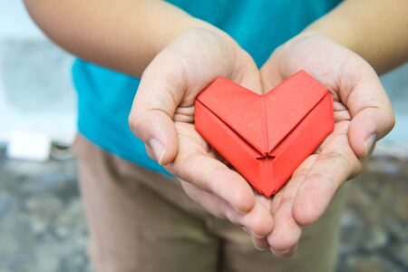 A red paper fold as heart shape in woman hand. A woman holding origami heart with two hand. Love and gift concept for valentine.の写真素材