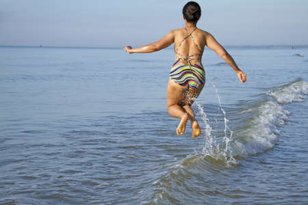 Lady with swimsuit happy high jump on wave at beach morning