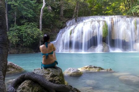 Traveler with blue swimsuit sit relax at Erawan Waterfall and natural in Kanchanaburi province Thailand.Erawan Waterfall Is a beautiful and famous water fall.の写真素材