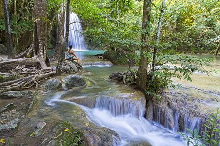 Woman in blue swimsuit sit look  Erawan Waterfall and natural in Kanchanaburi province Thailand.
Erawan Waterfall Is a beautiful and famous water fall.の写真素材