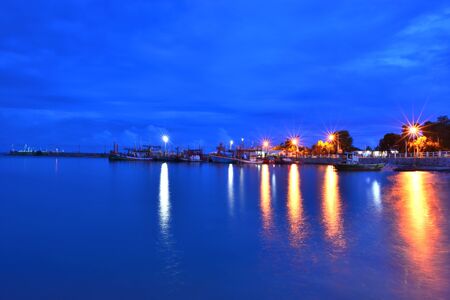 Light reflecting the water surface at night,along the coast and fishing boatsの写真素材