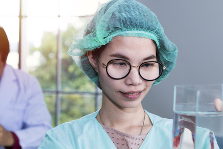 Woman veterinary student in green coat looking through fighting fish tank for research at laboratory.の写真素材