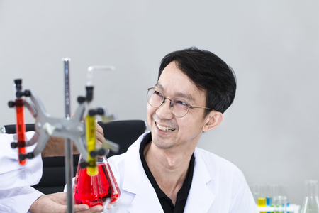 Senior handsome and smiling researcher talking with scientist about research near test tube at laboratory.Doctor in white suit and glasses .Copy space.の写真素材