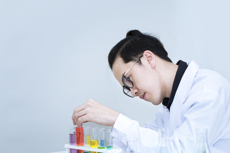 Young handsome medical student thinking and research with microscopes and color test tube.Doctor in whit suit and glasses.Copy space.の写真素材