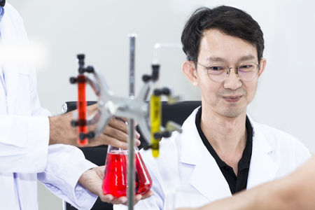 Senior handsome and smiling researcher talking with scientist about research near test tube at laboratory.Doctor in white suit and glasses .Copy space.の写真素材