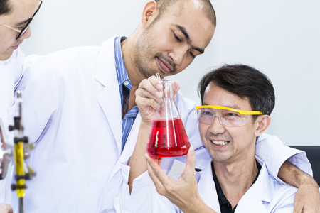 Portrait man of mature scientist and team in a white suit holding test tube at laboratory.の写真素材
