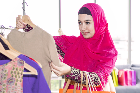 Young beautiful woman with shopping bags enjoying in shopping at clothing store.Lady in hijab choosing clothes. Copy space.の写真素材