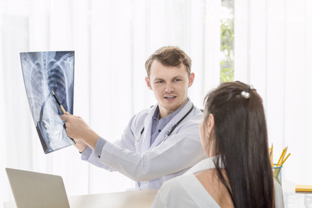 Medical professionals caucasian man holding xray and conversation with young woman Asia patient.Close up and copy space.の写真素材