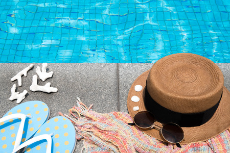 Concept of holiday tropical on summer, Accessories blue slippers, rainbow scarf, straw hat, shell, coral and sunglasses on border of a swimming pool. View from aboveの写真素材