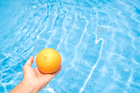 Concept of holiday tropical on summer, Blue wave pool and hand of a woman holding an orange.の写真素材