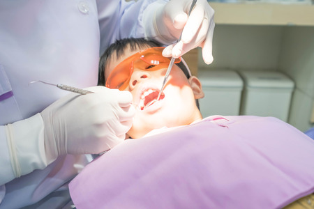 Real event photo, Cute little asian boy wearing glasses sitting in the dental chair and open him mouth during oral checkup with dentist To fill the tooth decay.の写真素材