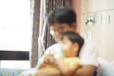 The boy wearing oxygen mask in hospital ward, boy's father's lap, blurの写真素材
