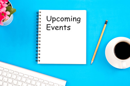 Concept Upcoming Events message on notebook with top viwe of modern workplace with office supplies, pencil, red flower, a cup of coffee and keyboard on blue background. Flat lay design.の写真素材