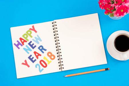 Top view of modern workplace with office supplies, pencil, red flower, a cup of coffee, on blue background. Flat lay design and happy new year 2018 wordsの写真素材