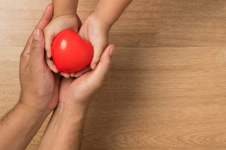 Concept of love in Valentine's Day. Father and son hands carries red heart to give love on a wooden floor.の写真素材