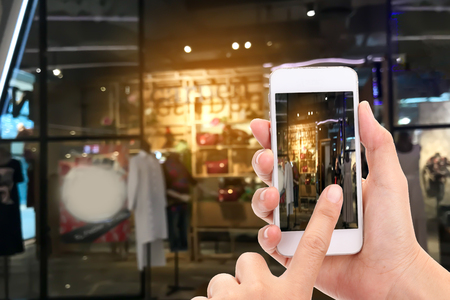 Woman hands Taking a picture with a smart phone in shopping mall with blurred image of clothes shop.の写真素材