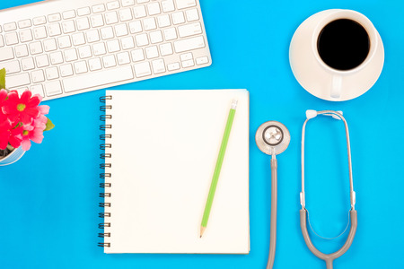 Top viwe of modern workplace with stethoscope and keyboard on blue table background. Flat lay design and copy space. Medical concept.の写真素材