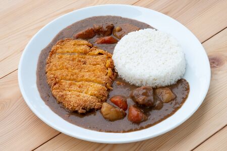 Tonkatsu, Japanese deep-fried pork cutlet on top with curry in white dish on wooden table. Japanese food.の写真素材