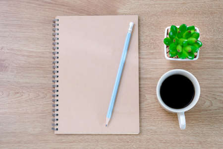 Notebook, pencil, Coffee cup and plastic cactus on wooden table background at coffee shop.