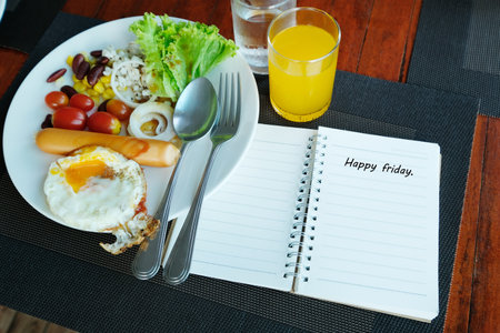 Happy friday message on notebook with breakfast set on wooden table.